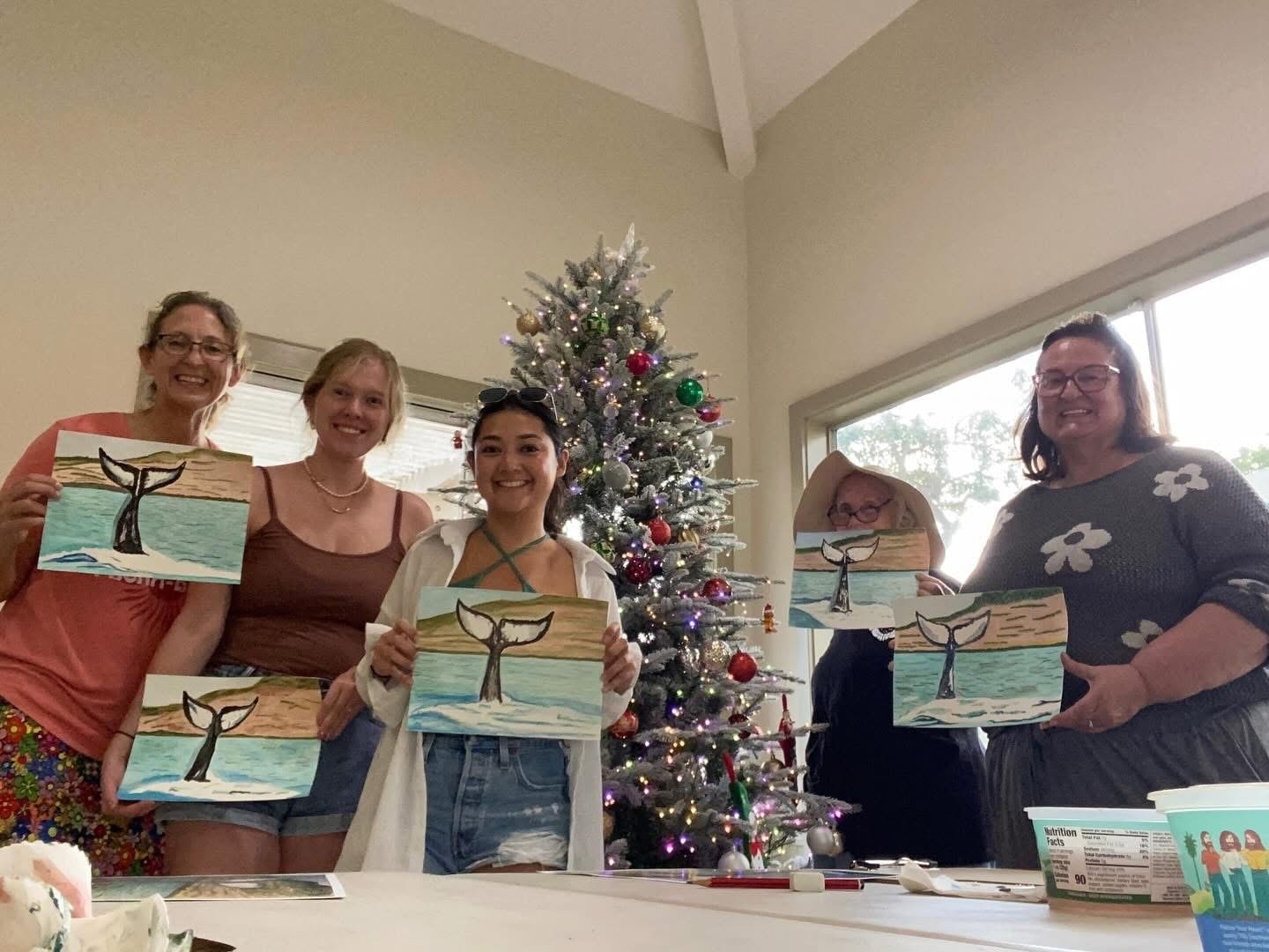 Group of adult students proudly displaying their whale tail watercolor paintings at a holiday class